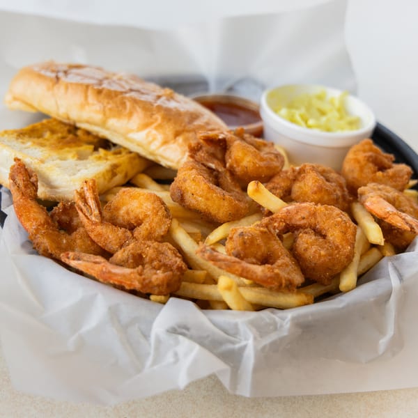 Fried shrimp and french fries in a basket with bread, coleslaw, and dipping sauce.