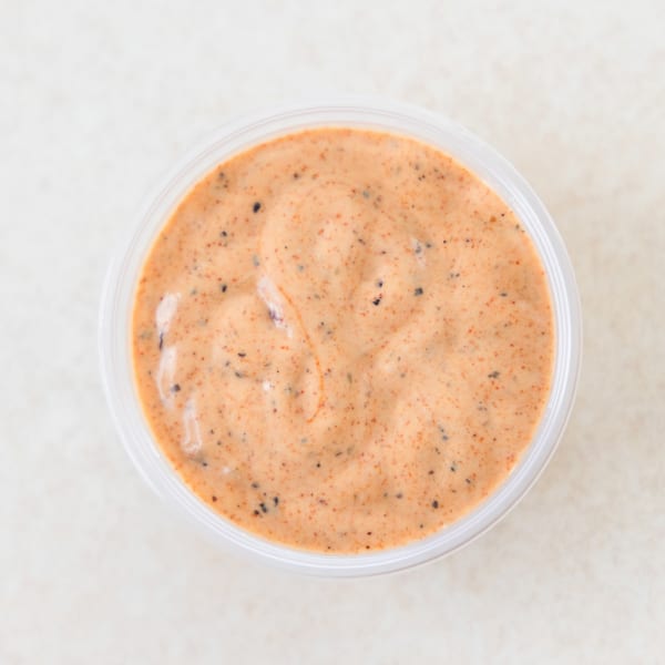 Overhead view of a small clear plastic cup filled with creamy orange sauce speckled with dark spices.