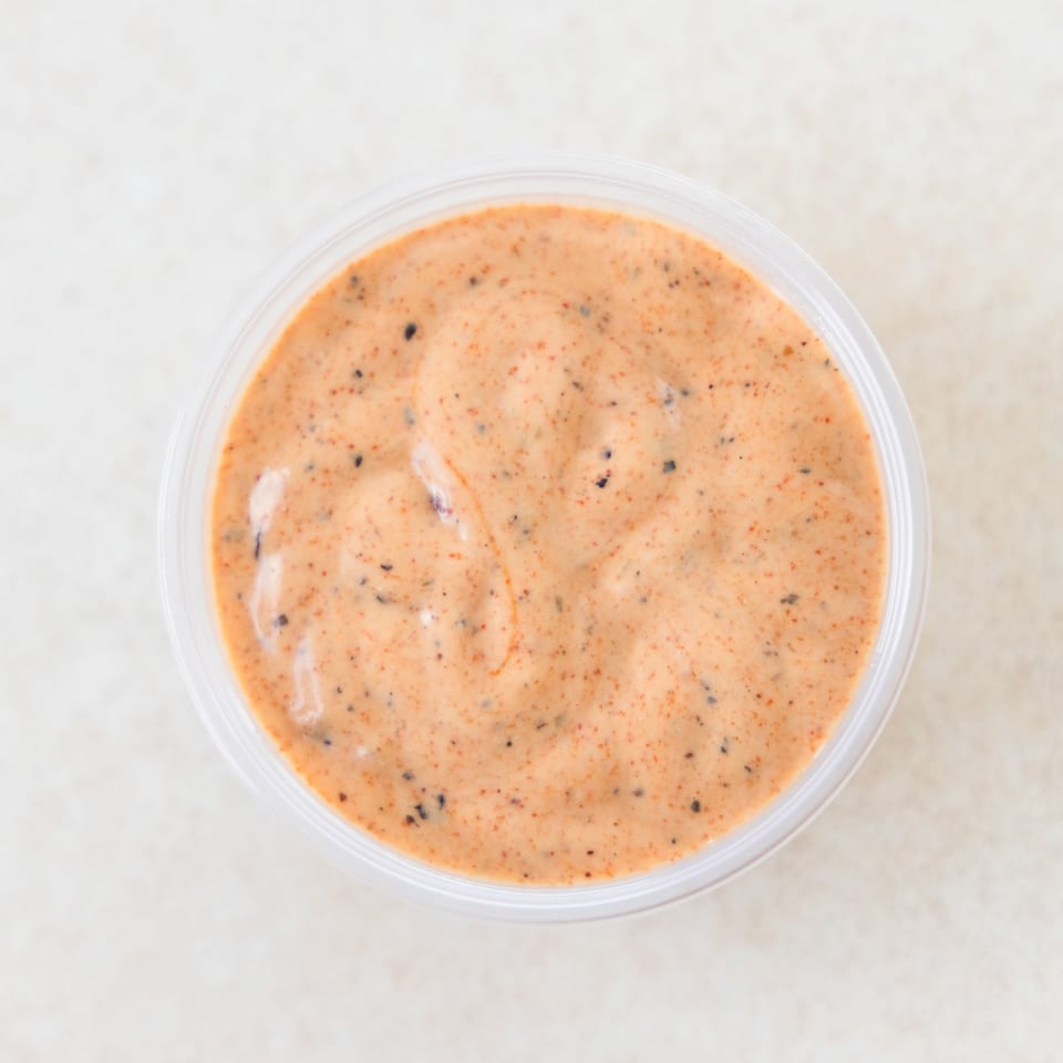 Overhead view of a small clear plastic cup filled with creamy orange sauce speckled with dark spices.