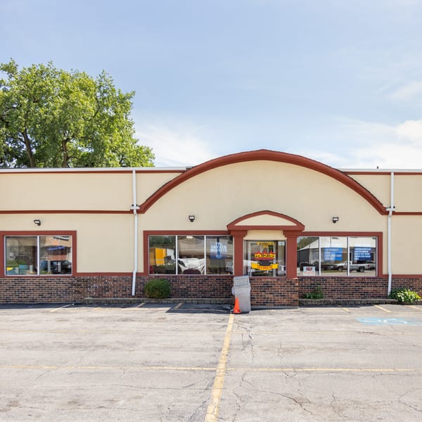 Exterior of King Gyro's restaurant with a beige facade, brick base, and a large parking lot.