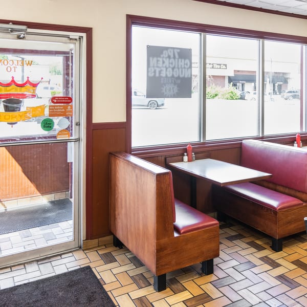 Interior of a fast-food restaurant with red booths, tables, and a glass door with delivery service stickers.