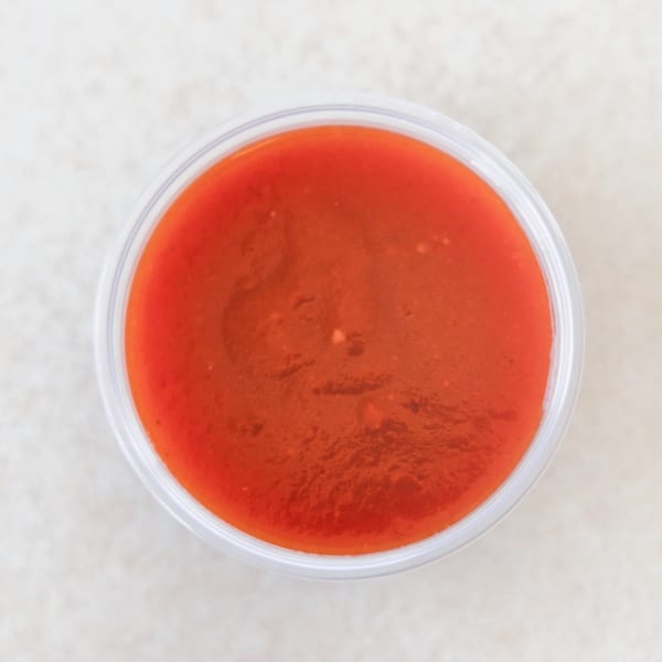 Overhead view of a small clear plastic cup filled with bright red sauce.