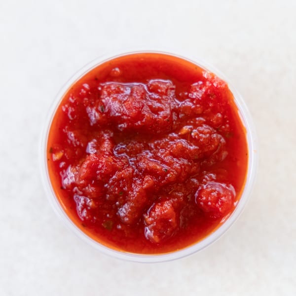 Overhead view of a small clear plastic cup filled with chunky red salsa.