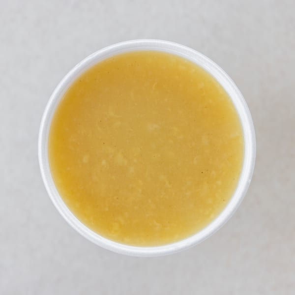 Overhead view of a white cup filled with a light yellow, creamy soup or sauce.