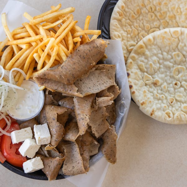A gyro platter with meat, fries, tomatoes, onions, feta, tzatziki, and pita bread.