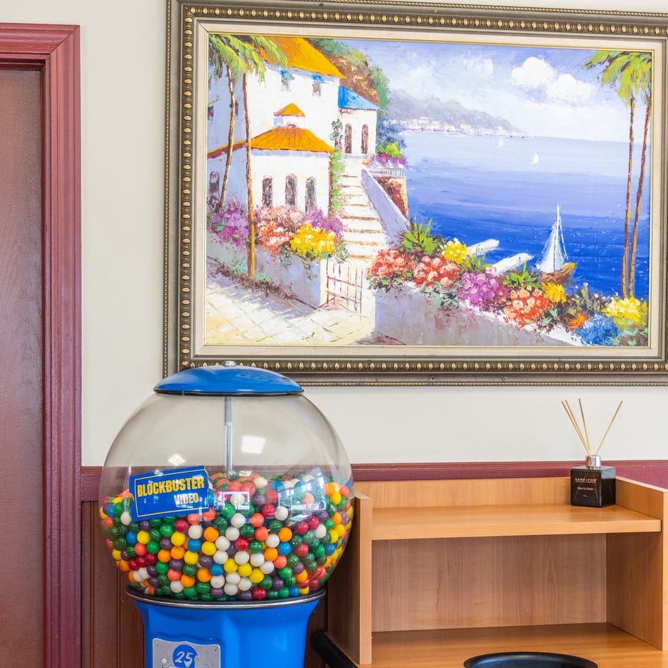 A gumball machine, a framed painting of a coastal town, and a wooden shelf with a diffuser.