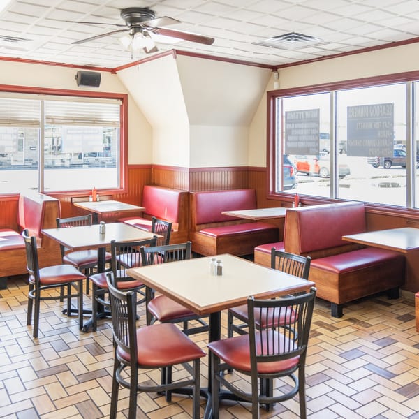 Empty diner interior with red booths, tables, chairs, and large windows looking out onto a street.