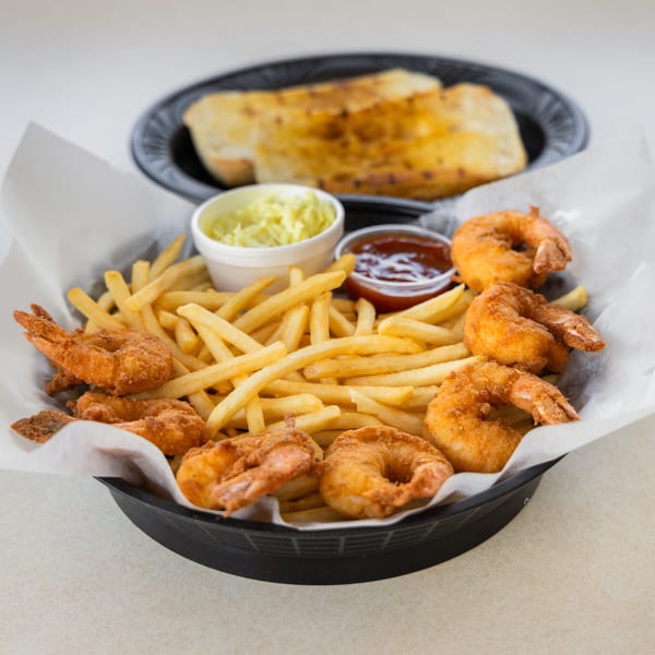 A basket of golden fried shrimp and french fries with ketchup, tartar sauce, and garlic bread.