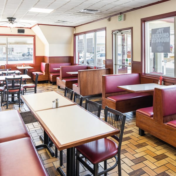 Empty diner interior with red booths, wooden tables, and tiled floors, seen through large windows.