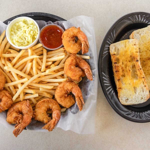 Fried shrimp and french fries with coleslaw, cocktail sauce, and grilled bread on a table.